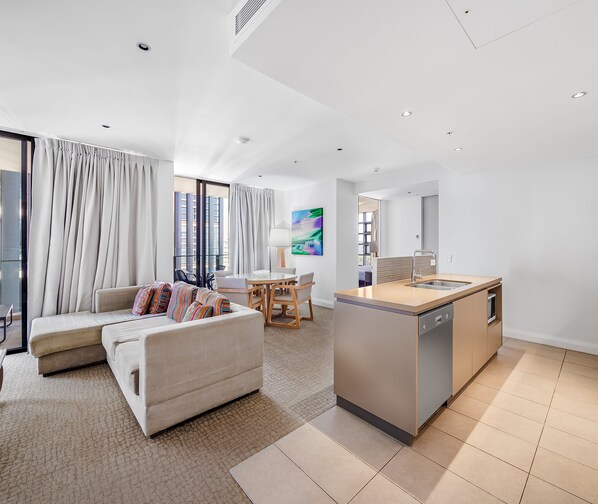A modern living room with a sofa, a dining table, and a kitchen area with a sink and stove.