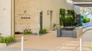 A modern building entrance with a stone facade, a sign reading "MONKOMO OAKS," and a covered outdoor area with plants and a water feature. - Oaks Redcliffe Mon Komo Suites (Redcliffe)