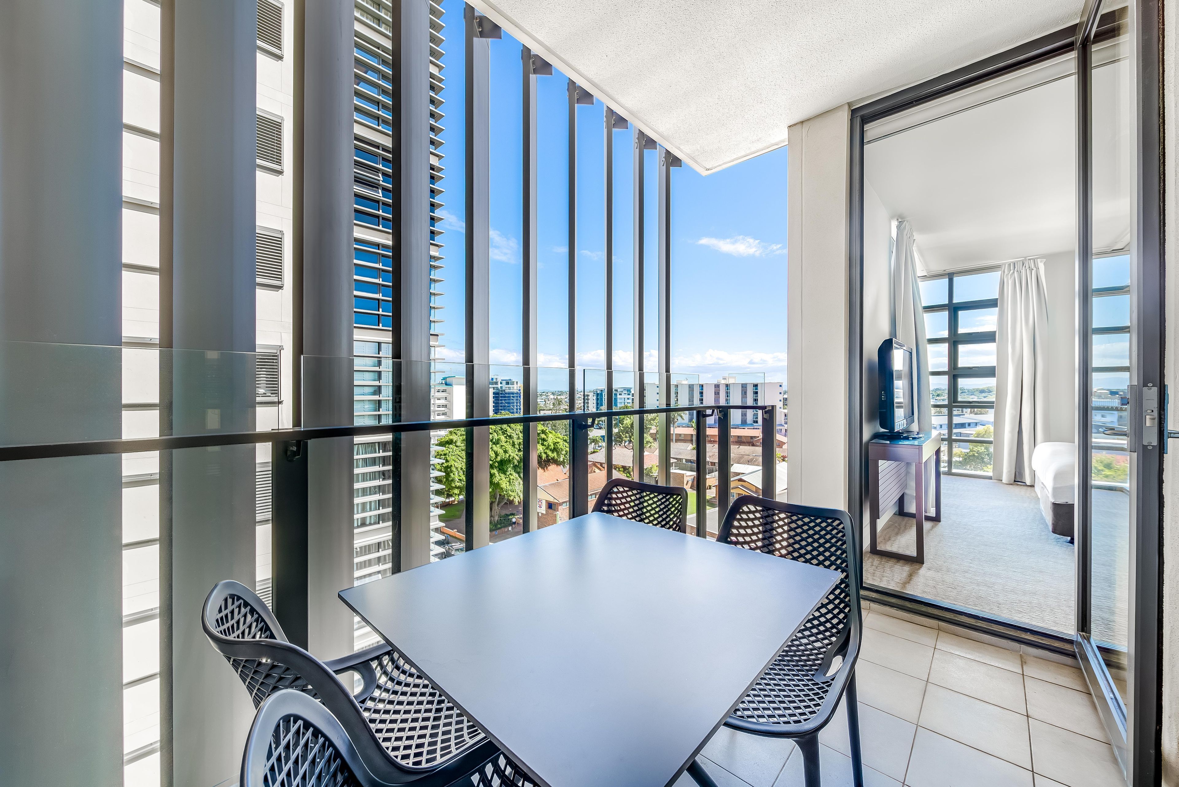 Ein Balkon mit Tisch und Stühlen, Blick auf die Stadtlandschaft und eine Schiebetür zu einem Innenraum.
