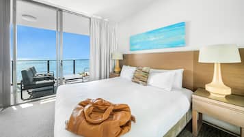 A hotel room with a bed, a nightstand, a lamp, a view of the sea, and a painting on the wall.
