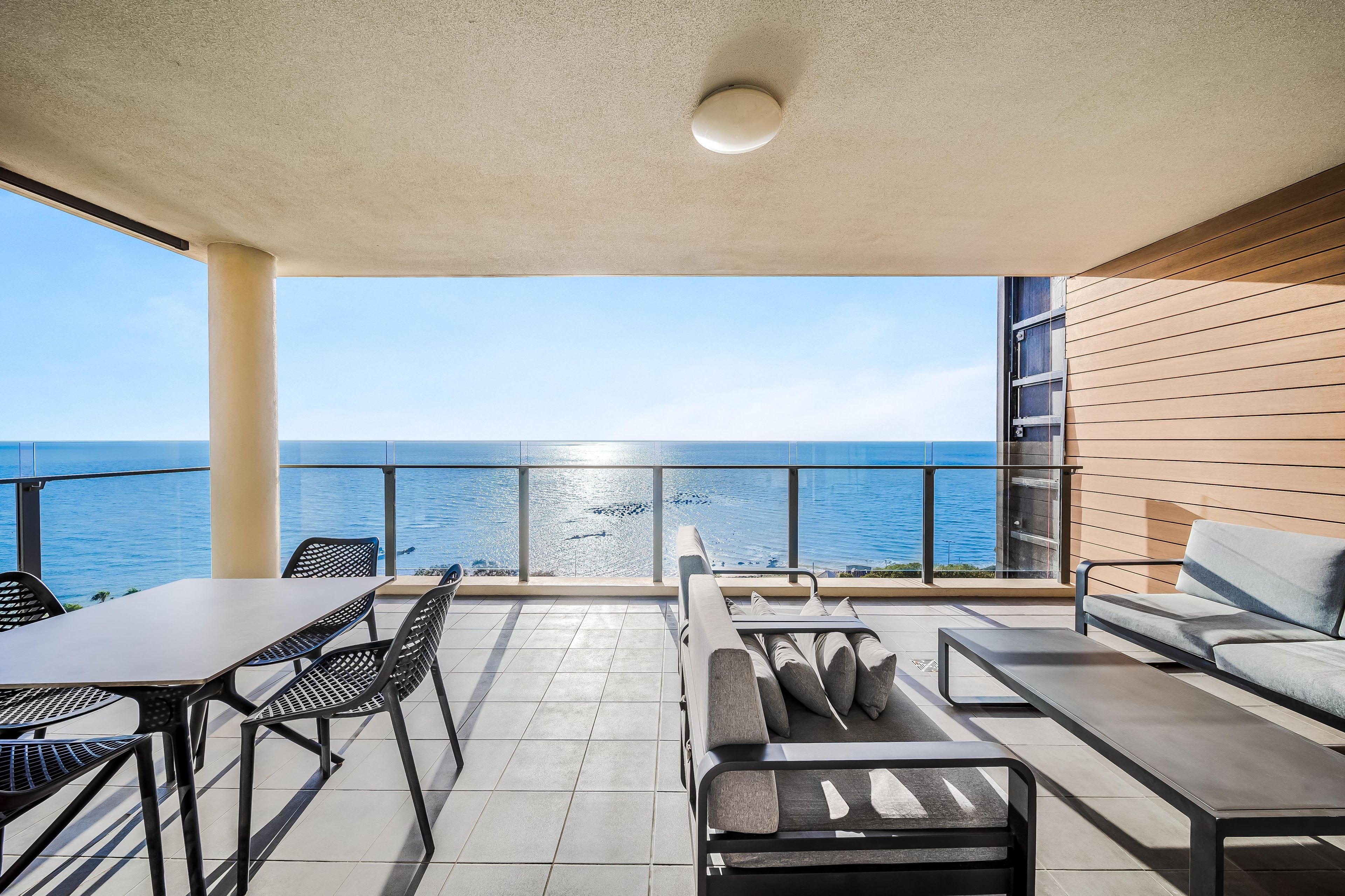 A balcony with a view of the sea, furnished with a table, chairs, and a sofa.