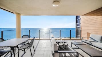 A balcony with a view of the sea, furnished with a table, chairs, and a sofa.