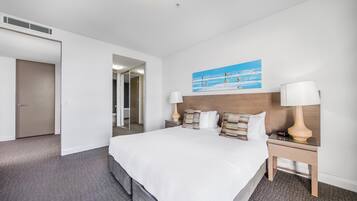 Habitación de hotel con una cama grande, dos mesitas de noche, una mesita auxiliar, un cuadro y una puerta que da a un baño.
