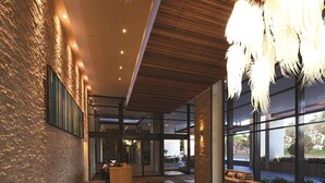 A modern lobby with a wooden reception desk, a seating area with a bench, and large windows offering views of the outdoors.