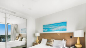 A hotel room with a large bed, two bedside tables with lamps, a painting on the wall, and a large window with curtains. - Oaks Redcliffe Mon Komo Suites (Redcliffe)
