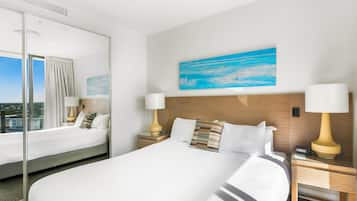 Quarto de hotel com uma cama grande, duas mesas de cabeceira com luminárias, um quadro na parede e uma janela ampla com cortinas.