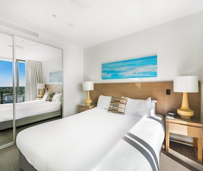 A hotel room with a large bed, two bedside tables with lamps, a painting on the wall, and a large window with curtains.