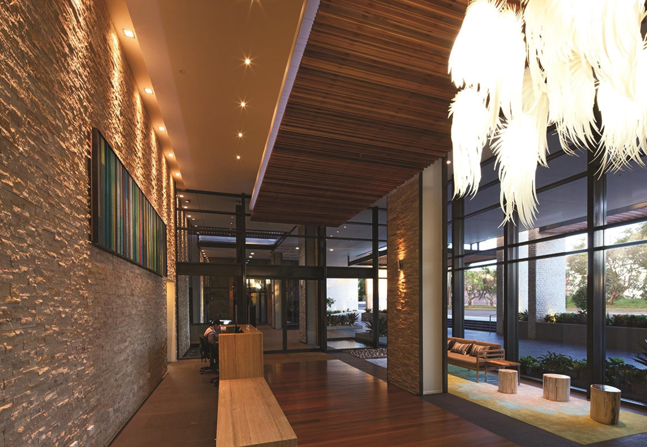 A modern lobby with a wooden reception desk, large windows, and a hanging light fixture.