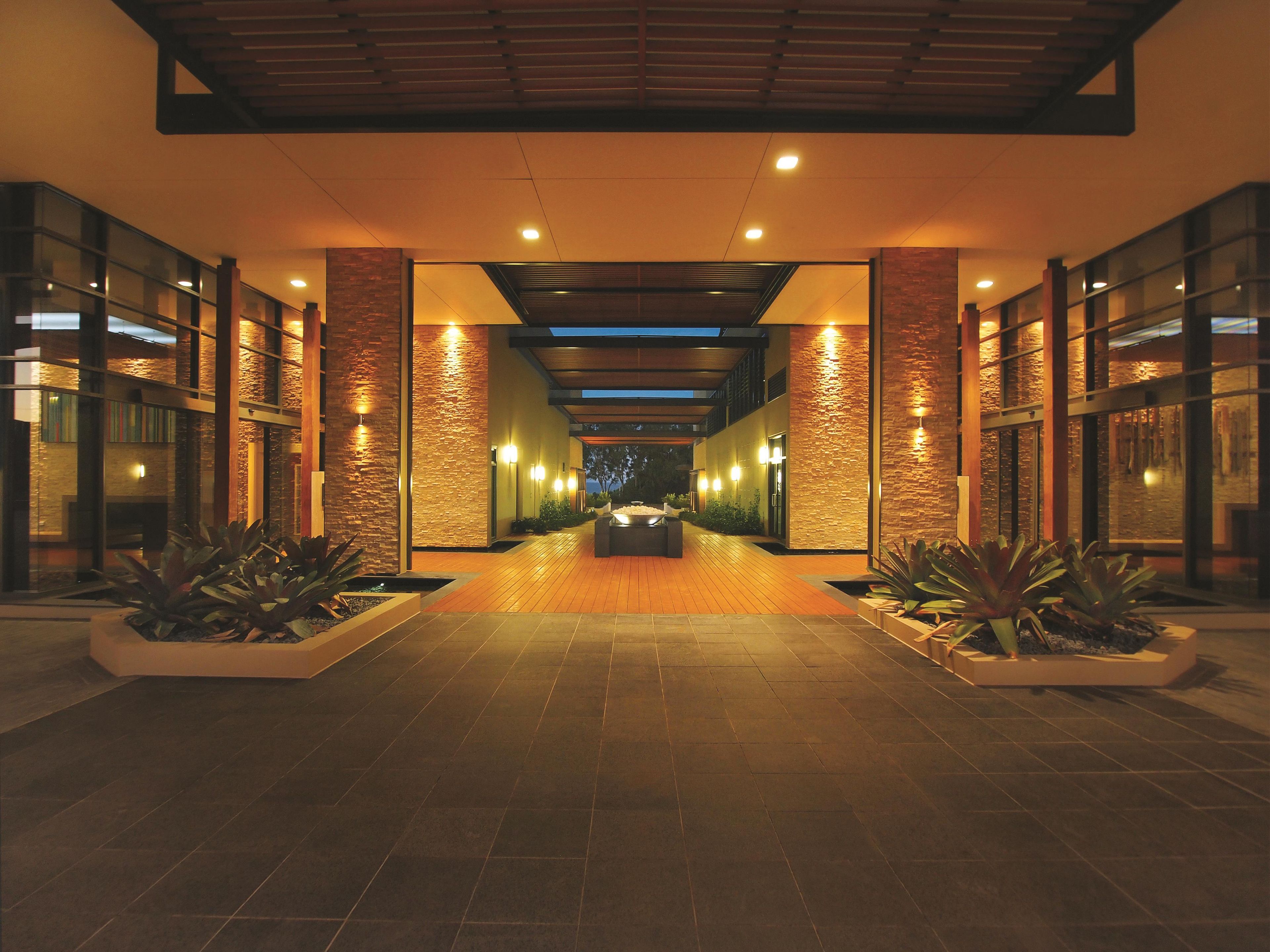 A modern hotel corridor with a central seating area, flanked by glass walls and stone accents.