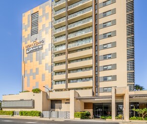 A modern hotel building with a geometric facade, multiple balconies, and a prominent sign. - Oaks Redcliffe Mon Komo Suites (Redcliffe)