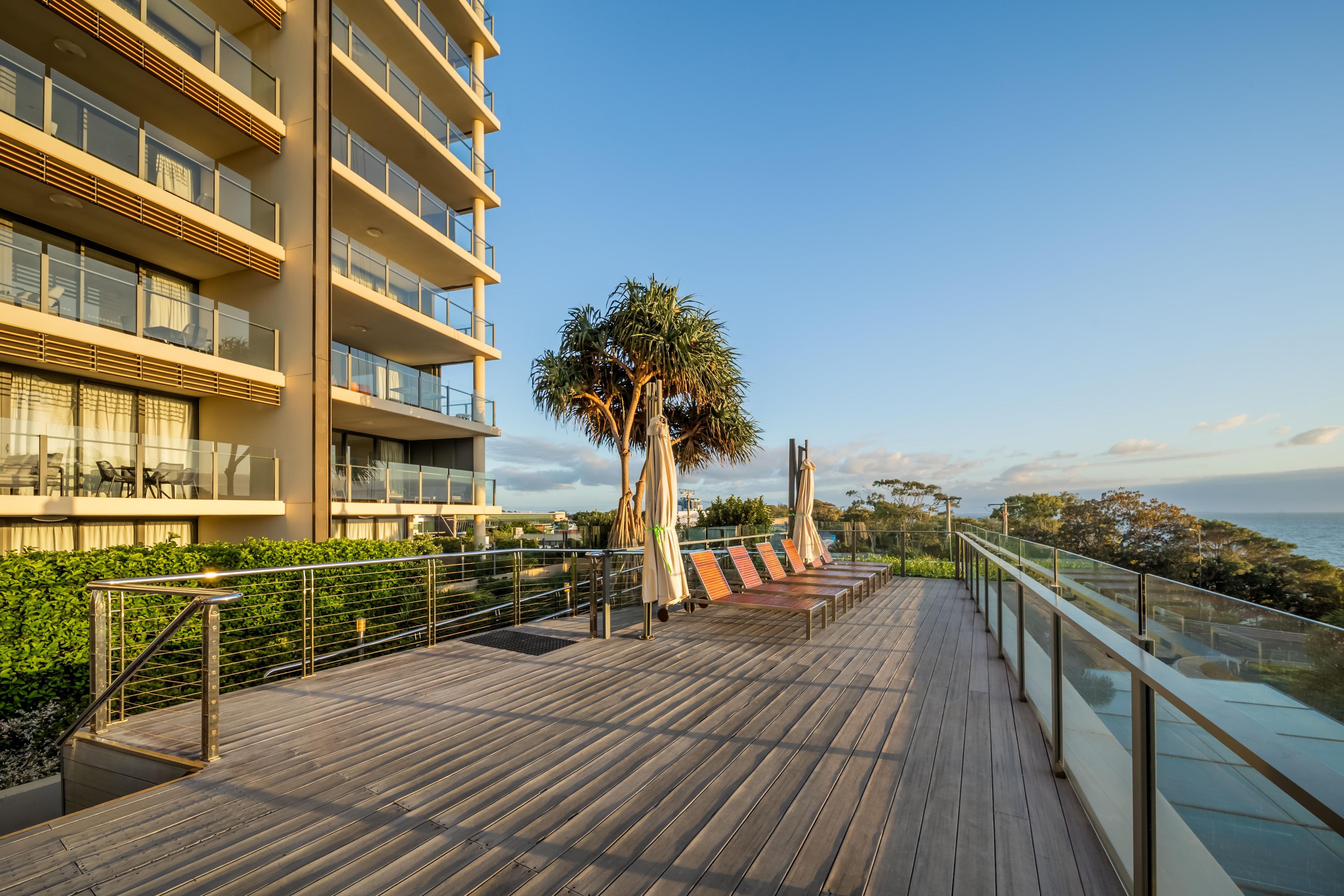 A modern hotel balcony with a wooden deck, glass railings, and a view of the sea.