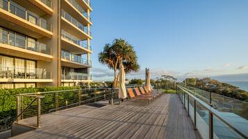 A modern hotel balcony with a wooden deck, glass railings, and a view of the sea.