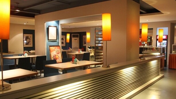 A modern restaurant with a long counter, tables, and chairs. - Jinjiang Inn East Shanghai New International Exhibition Ctr (Shanghai)