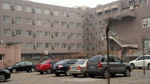 Uma área de estacionamento com vários carros estacionados em frente a um edifício com vários andares, janelas e aparelhos de ar condicionado.