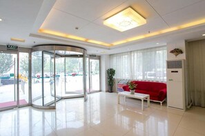 A hotel lobby with a revolving door, a red sofa, a white table, and a potted plant. - Jinjiang Inn Olympic Park (Beijing)