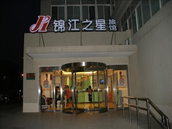 A hotel entrance with a glass revolving door, a sign with Chinese characters, and a metal staircase leading up to the entrance.
