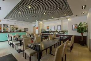 A restaurant with a grid-patterned ceiling, multiple dining tables, chairs, a bar area, and a potted plant. - Jinjiang Inn Olympic Park (Beijing)