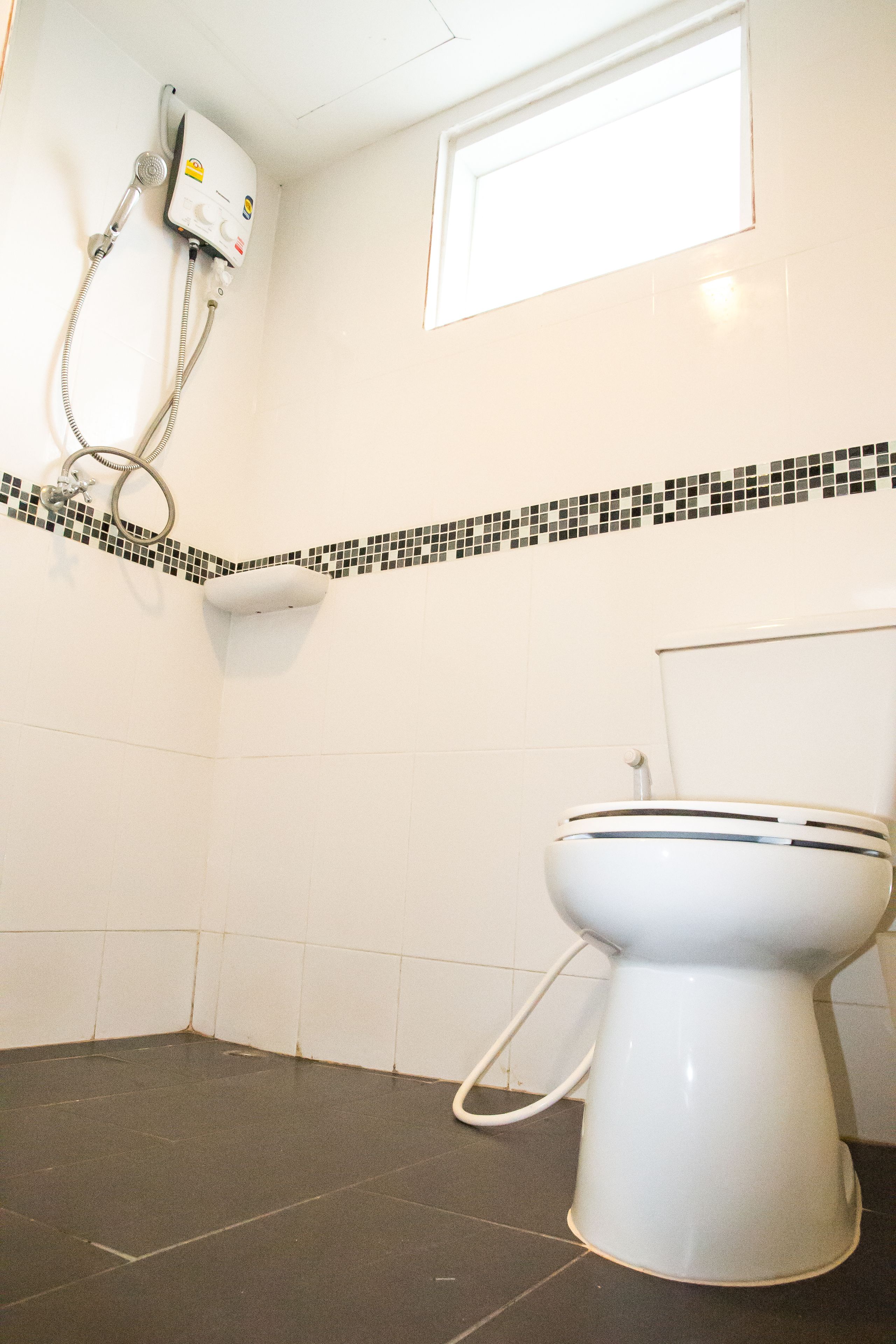 A bathroom with a toilet, a shower unit, and a small window.