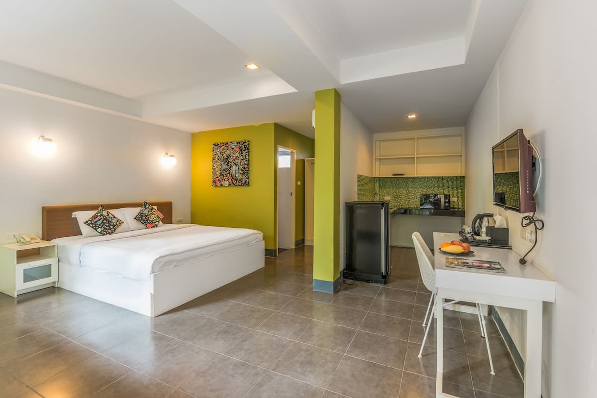 Une chambre d’hôtel comprenant un lit, une table de chevet et un bureau avec une chaise. Il y a également un coin cuisine équipé d’un réfrigérateur et d’un four à micro-ondes.