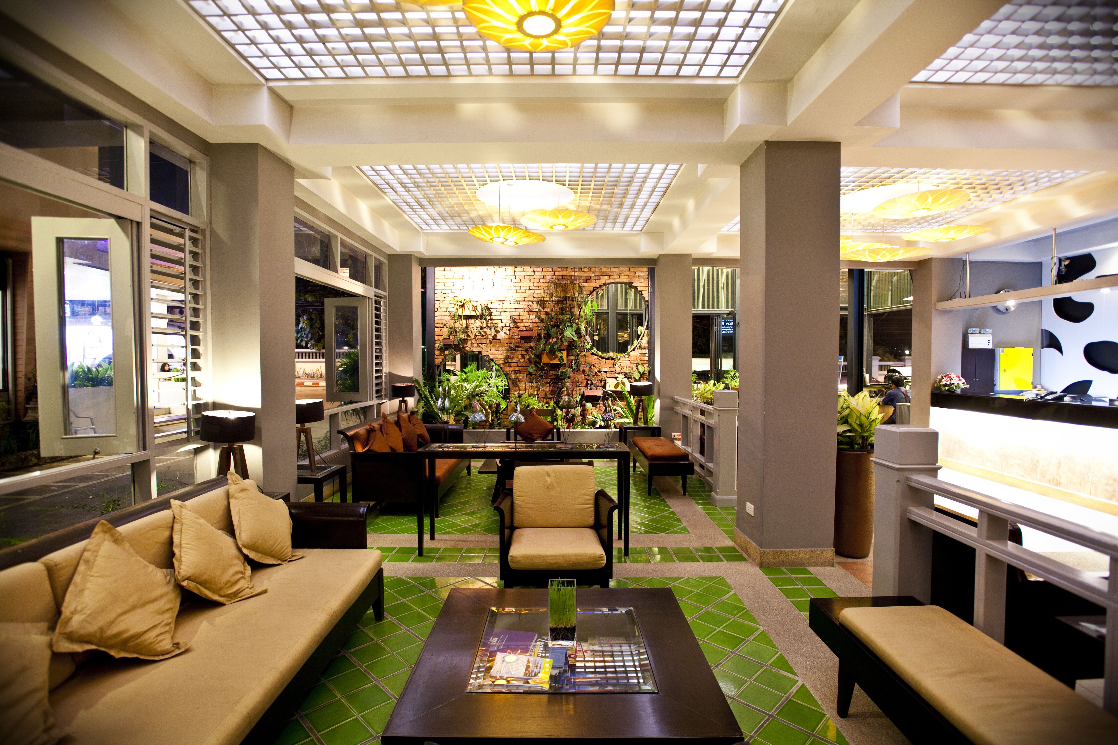 A modern lobby with a green-tiled floor, a sofa, a coffee table, and a brick wall with plants.