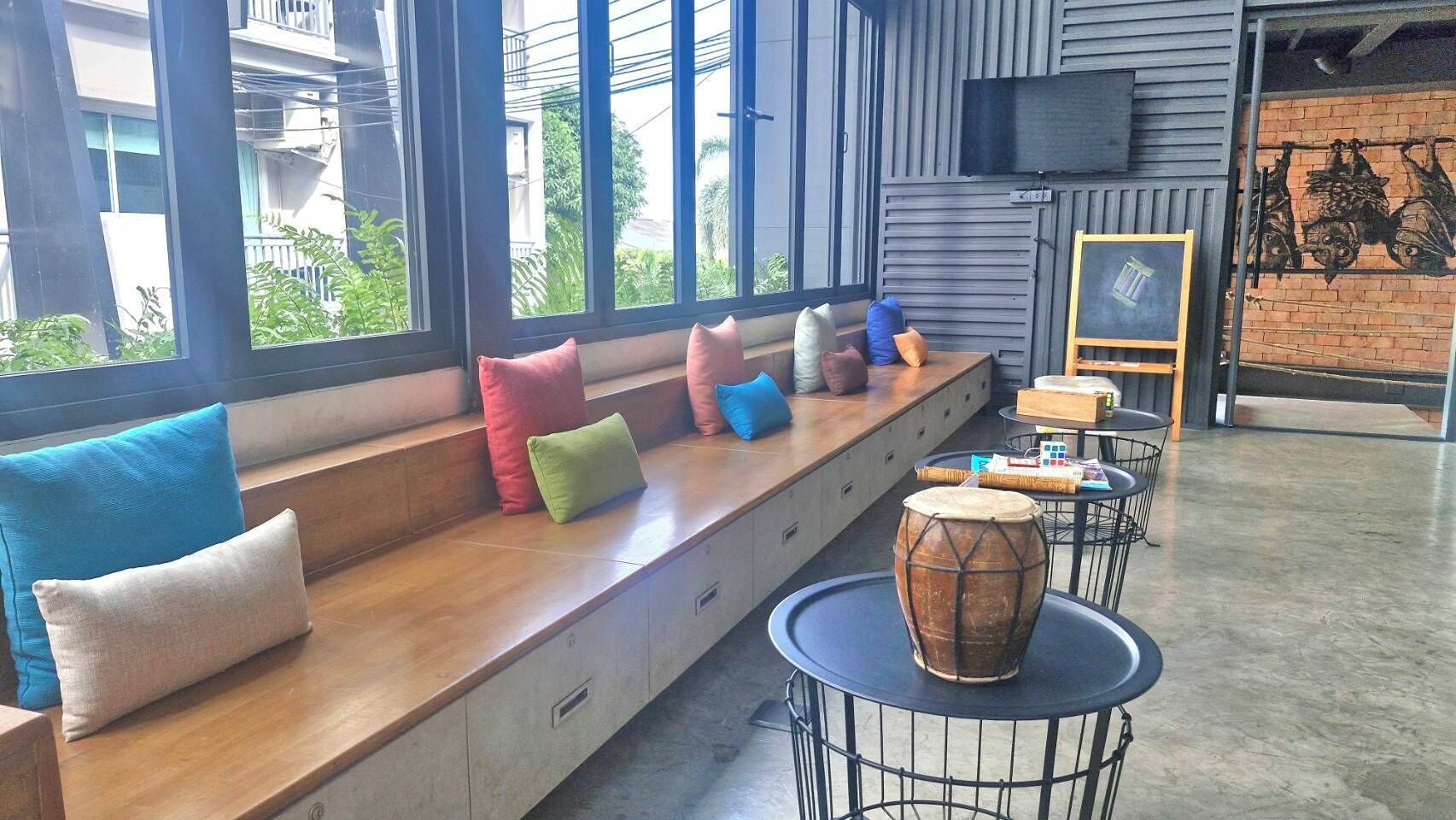 A seating area with colorful cushions, a drum, and a television on the wall.