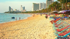 A beach with rows of colorful beach chairs, a sandy shore, and a city skyline in the background.