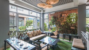 A modern indoor seating area with a sofa, tables, and chairs, featuring a brick wall and large windows.