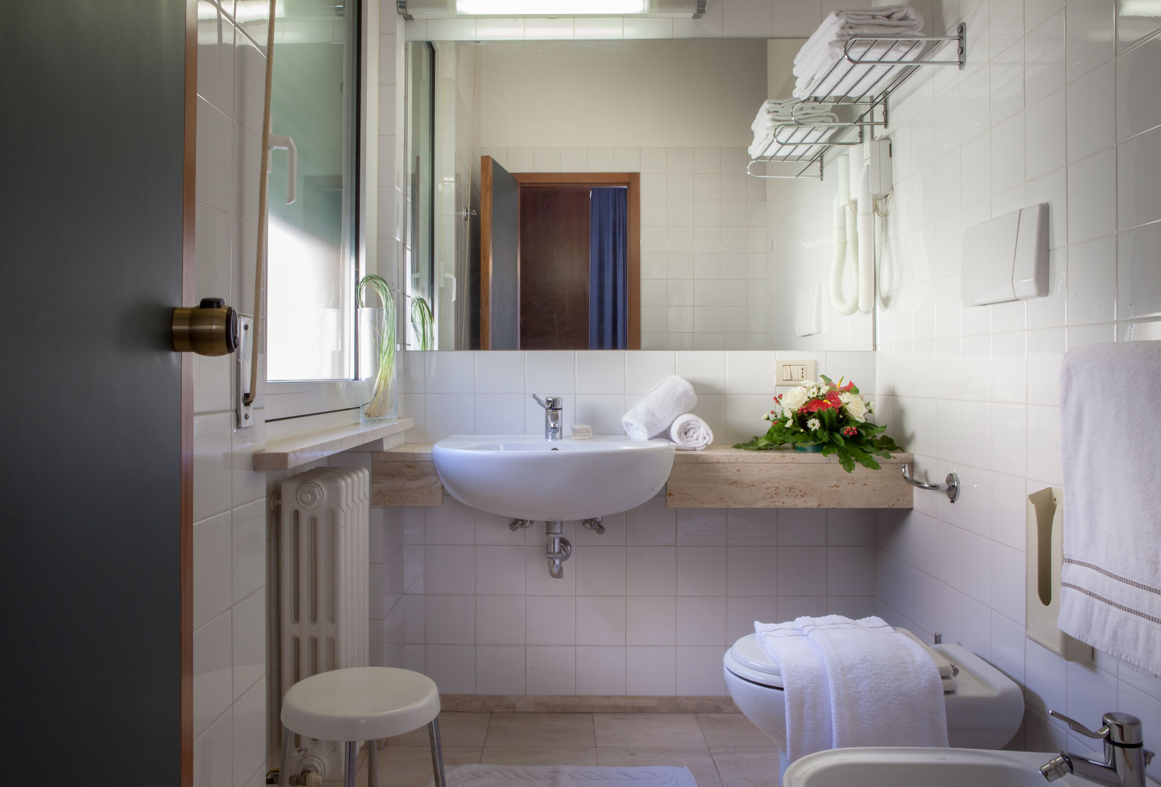 Et moderne badeværelse med en hvid vask, toilet og badekar. Der er et vindue med udsigt, og en håndklædestang over vasken.