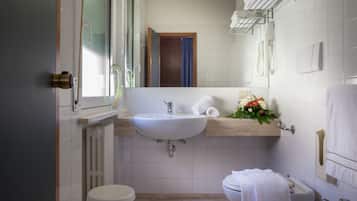 Et moderne badeværelse med en hvid vask, toilet og badekar. Der er et vindue med udsigt, og en håndklædestang over vasken.