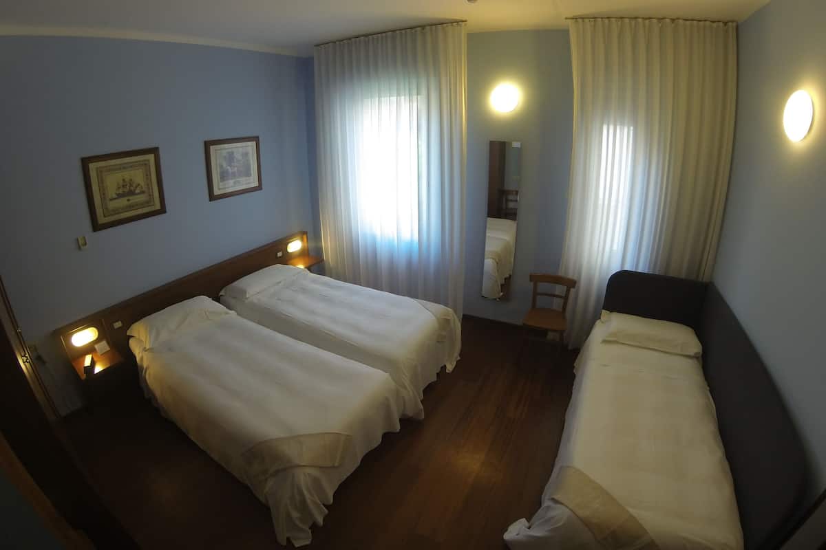 Habitación de hotel con dos camas individuales, piso de madera, una pequeña silla, un espejo y dos cuadros en la pared.