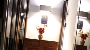 A hotel lobby with a wooden cabinet, a vase with flowers, and a doormat with a logo.