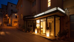 A hotel with a restaurant named "MARAMMI" at the entrance, featuring a glass facade and potted plants.