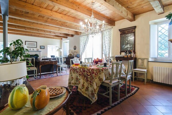 A spacious dining area with a wooden ceiling and a chandelier, a table set for a meal, and a view of the outdoors through a window.
