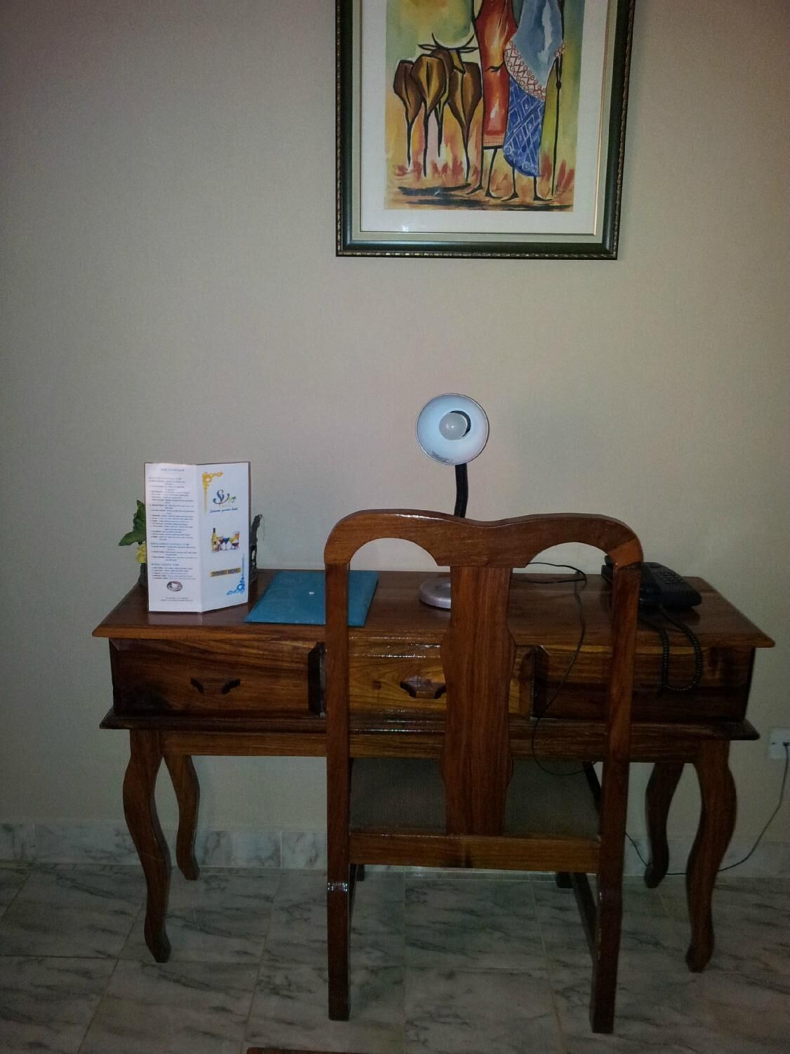 Un escritorio de madera con una silla, un cuadro enmarcado en la pared y una lámpara de escritorio.