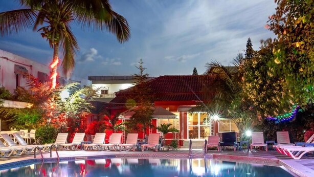 Ein Swimmingpool mit Liegestühlen, Palmen und einem Gebäude mit roten Ziegeln.