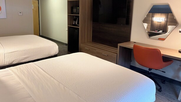 Habitación de hotel con dos camas, un escritorio, una silla, un televisor, un microondas y un armario.