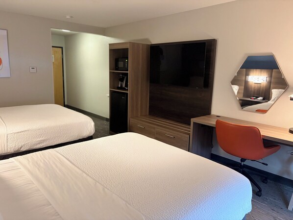 Een hotelkamer met twee bedden, een bureau, een stoel, een televisie, een magnetron en een kledingkast.