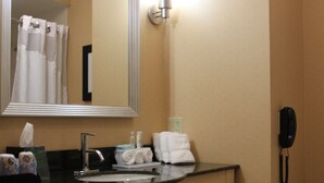 Un baño de hotel con tocador de madera, un espejo grande, un lavabo, un perchero para toallas, un teléfono y un dispensador de papel higiénico.