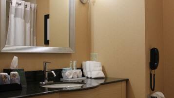 A hotel bathroom with a wooden vanity, a large mirror, a sink, a towel rack, a phone, and a toilet paper holder.