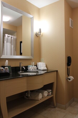 Een hotelbadkamer met een houten wastafel, een grote spiegel, een wastafel, een handdoekhouder, een telefoon en een toiletrolhouder.