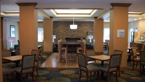 A hotel dining area with multiple tables and chairs, a stone wall, and a ceiling with recessed lighting. - Holiday Inn Express Cortland by IHG (Cortland)