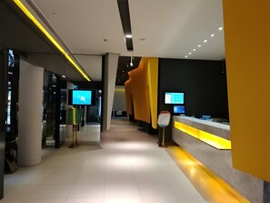 Um hall de hotel moderno com uma mesa de recepção, telas digitais e um design limpo e minimalista.