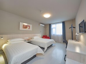Quarto de hotel com duas camas, uma cadeira vermelha, uma escrivaninha com abajur e uma janela grande com cortinas.