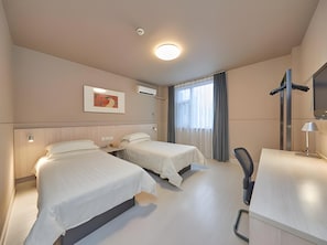 Quarto de hotel com duas camas, uma escrivaninha, uma cadeira, televisão e um quadro na parede.
