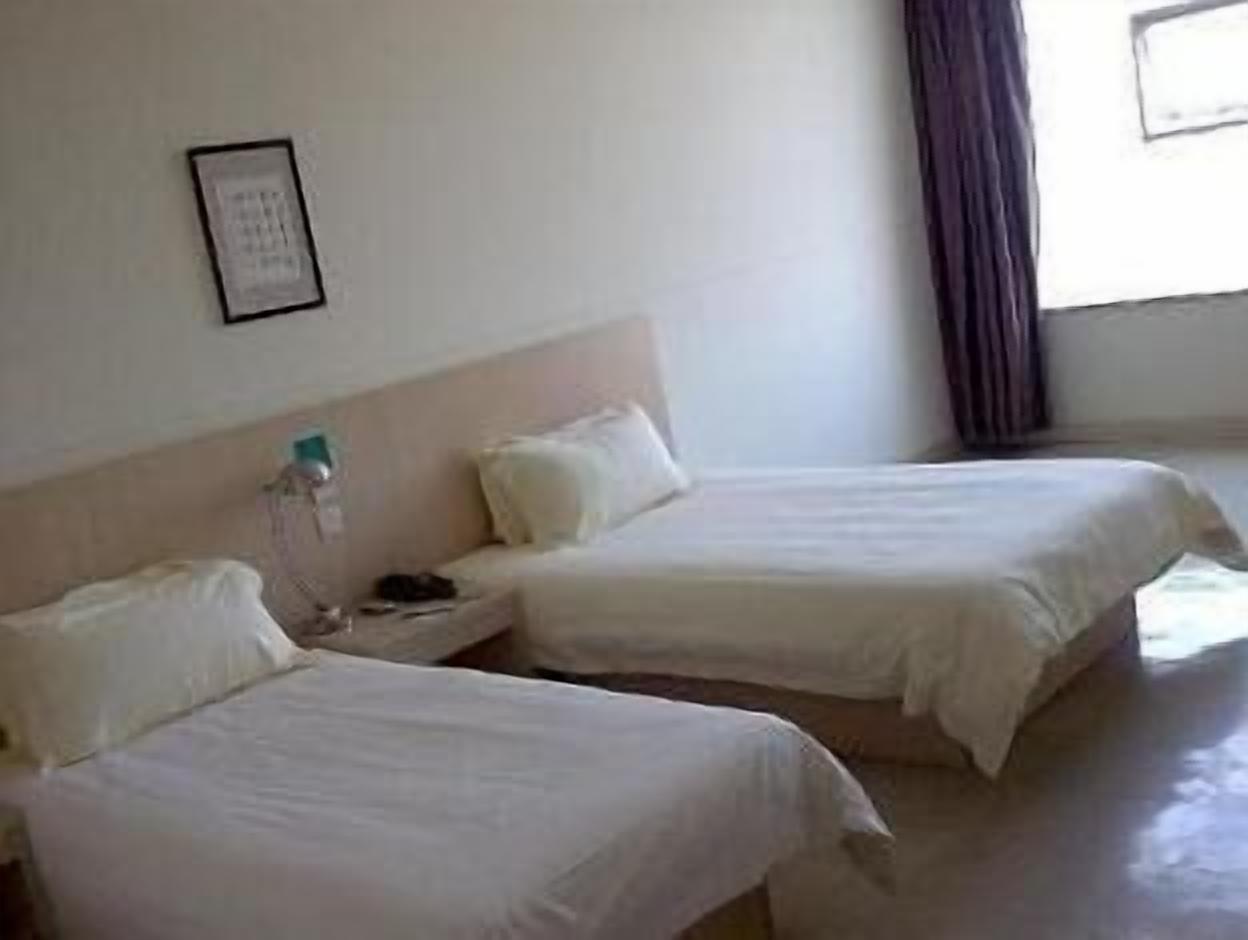 A hotel room with two single beds, a bedside table with a lamp, a framed picture on the wall, and a window with curtains.