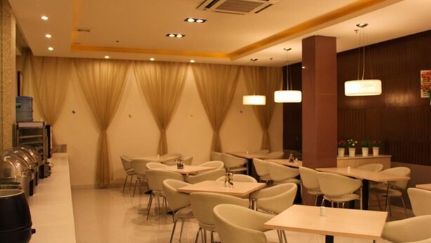 Restaurante com várias mesas e cadeiras, um buffet com estações de comida cobertas, e uma atmosfera acolhedora e com iluminação suave.