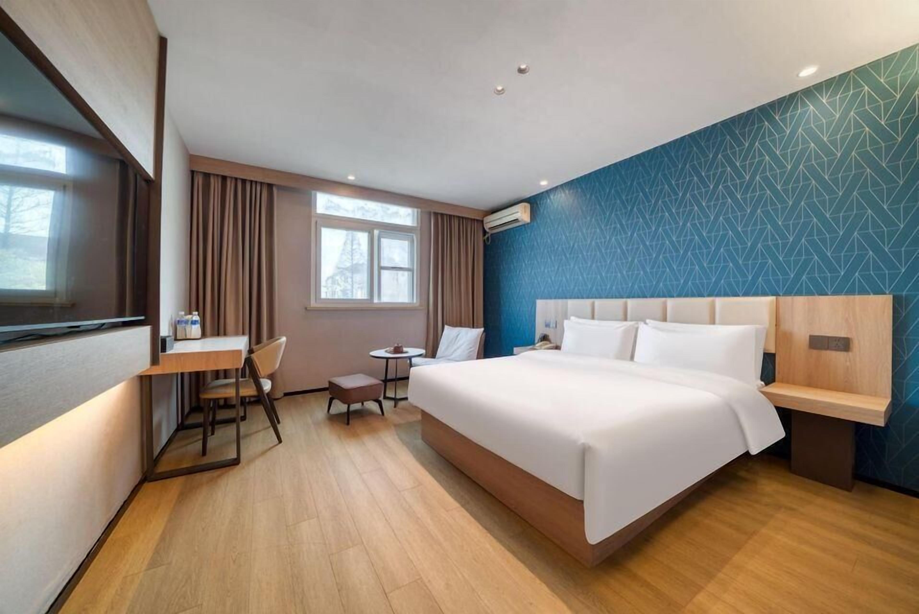 A hotel room with a large bed, a desk, a chair, a small table, and a window.