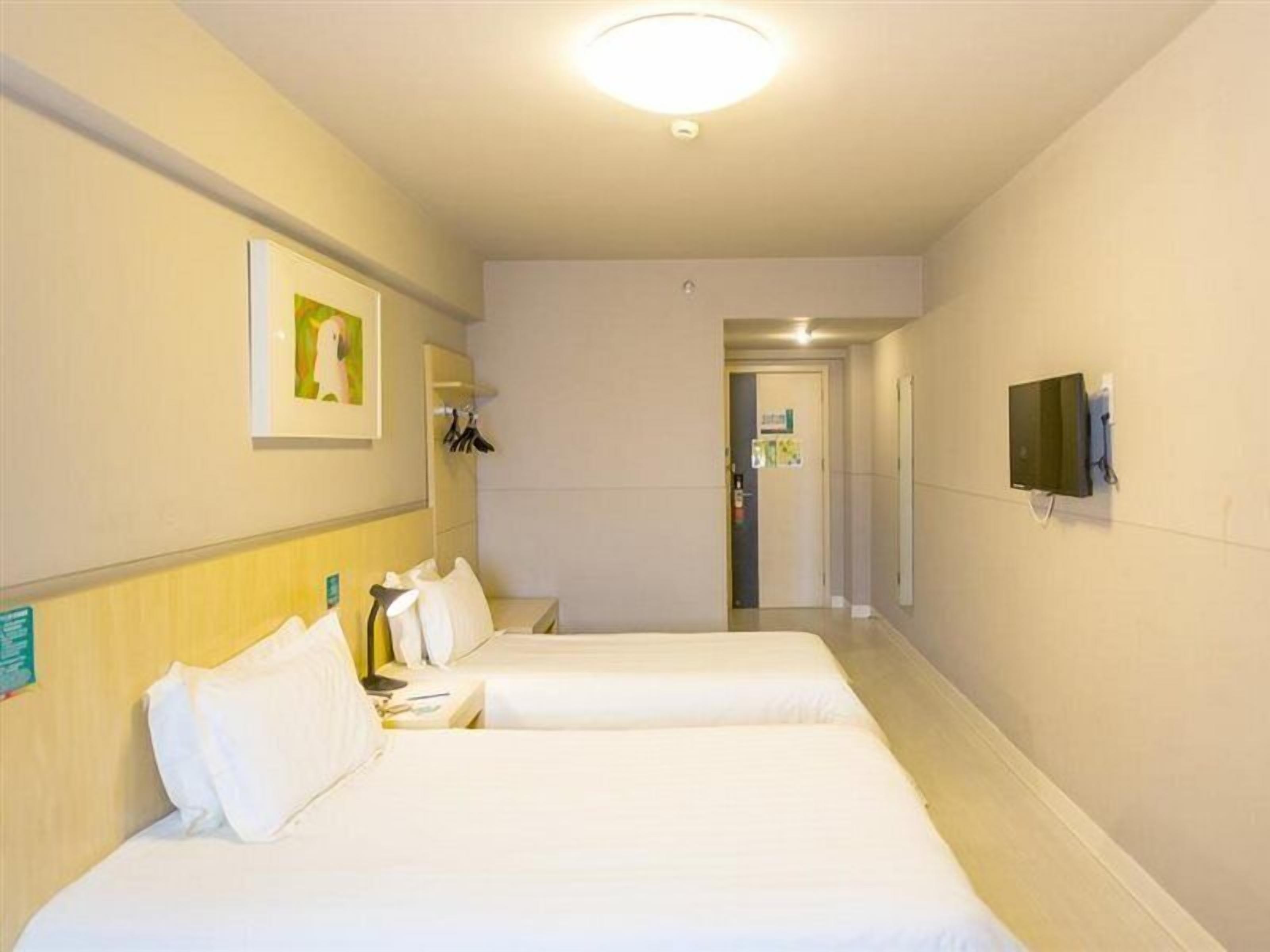 A hotel room with two beds, a TV, and a door leading to a hallway.