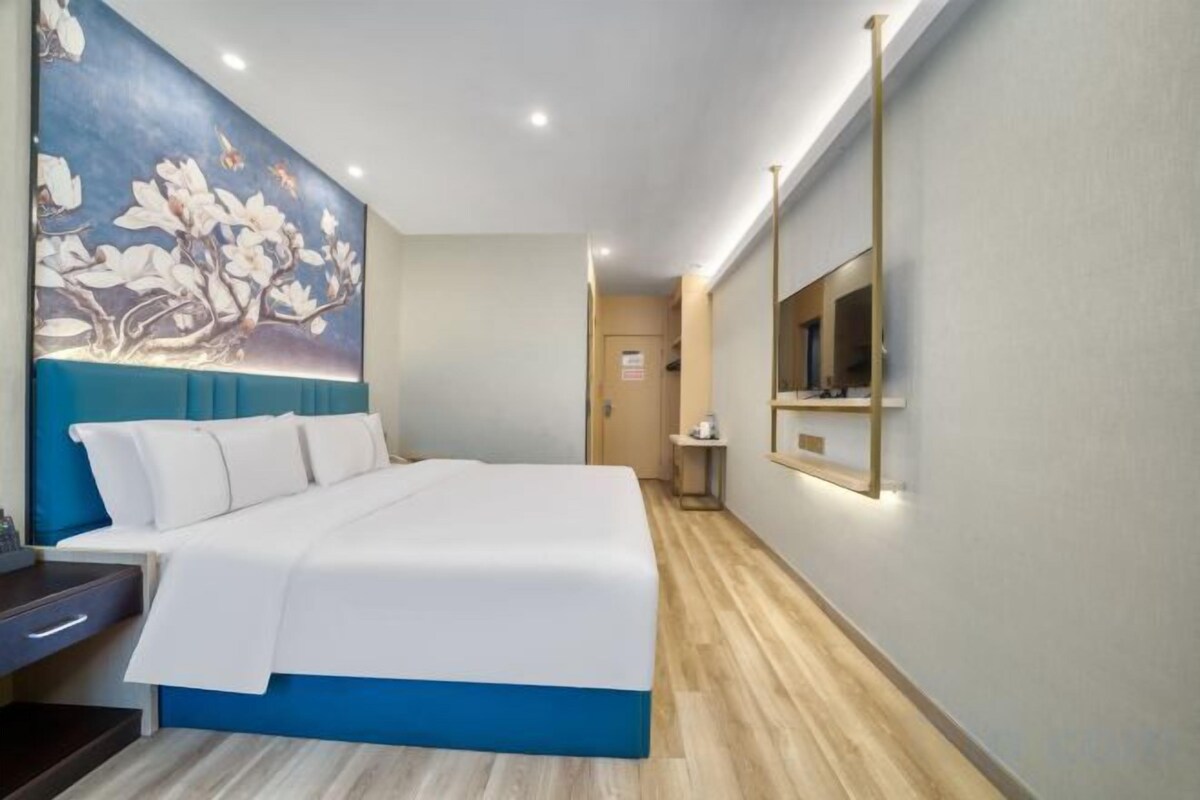 Een hotelkamer met een bed, een schilderij aan de muur, een spiegel en een houten vloer.