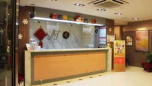 Uma área de recepção de hotel com balcão de mármore, uma coroa de Natal e uma placa com a inscrição 'Merry Christmas'.